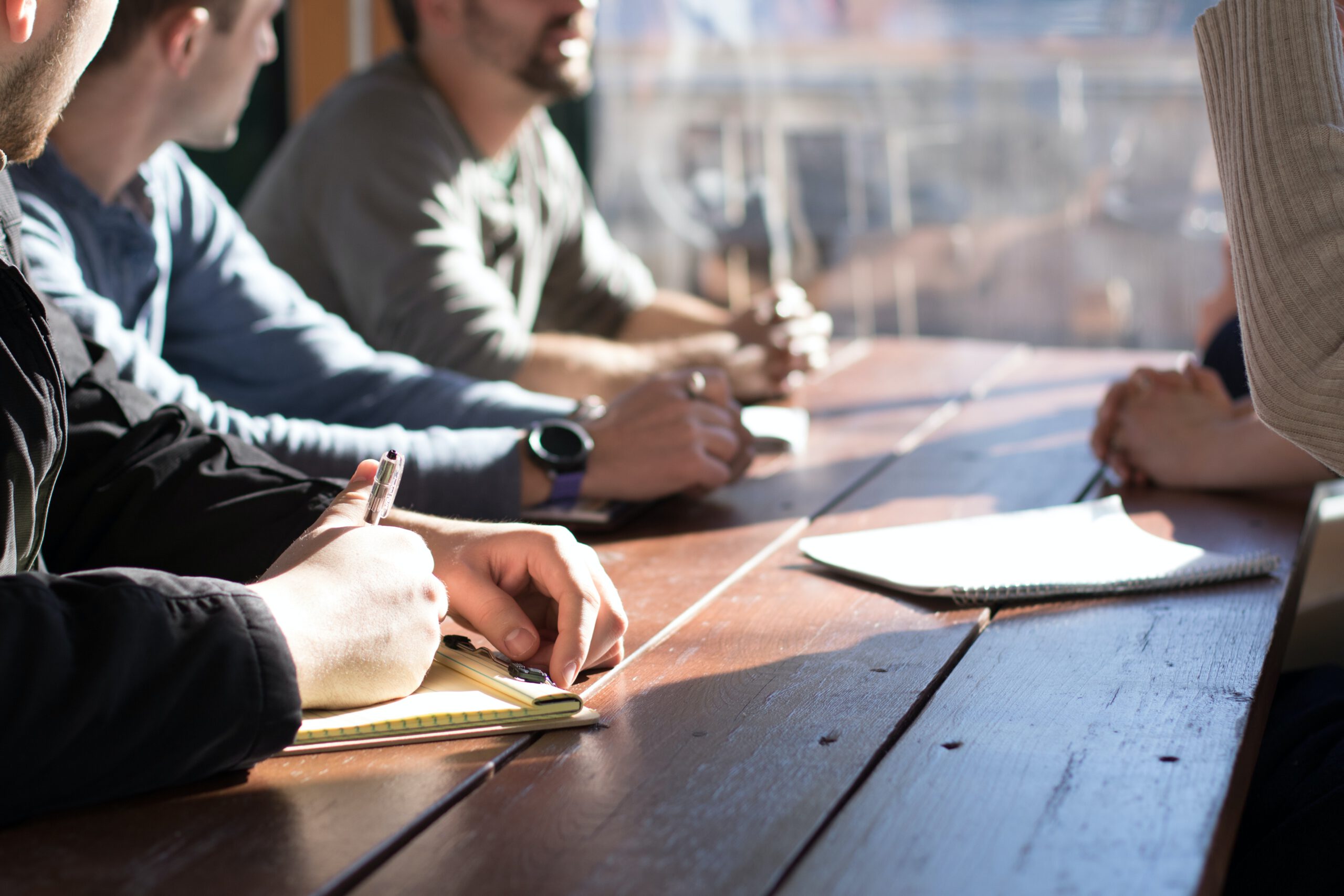 Mehrere Personen sitzen am Tisch, beraten sich und schreiben auf Papier mit, Sprechen und coachen sich gegenseitig